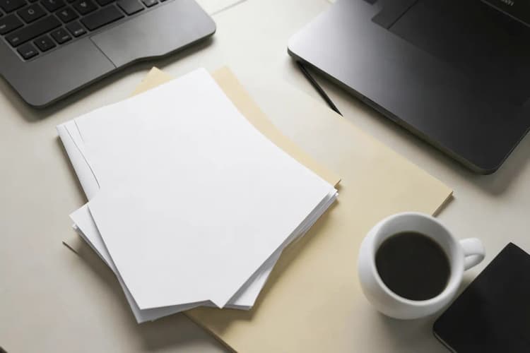 Uma pessoa analisando relatórios em uma mesa com um laptop e um café.