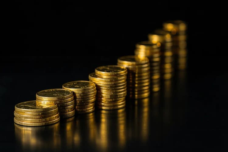 Um gráfico de linha ascendente feito de moedas de ouro empilhadas, em uma superfície escura.