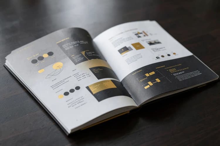 Um portfólio aberto mostrando exemplos de trabalhos de design gráfico e campanhas de marketing digital em páginas de um livro grosso.