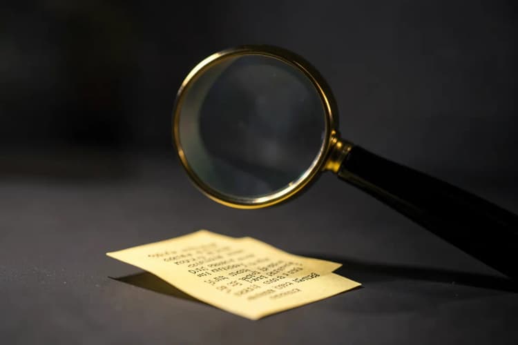 Uma lupa examinando um pequeno pedaço de papel com um texto ilegível.