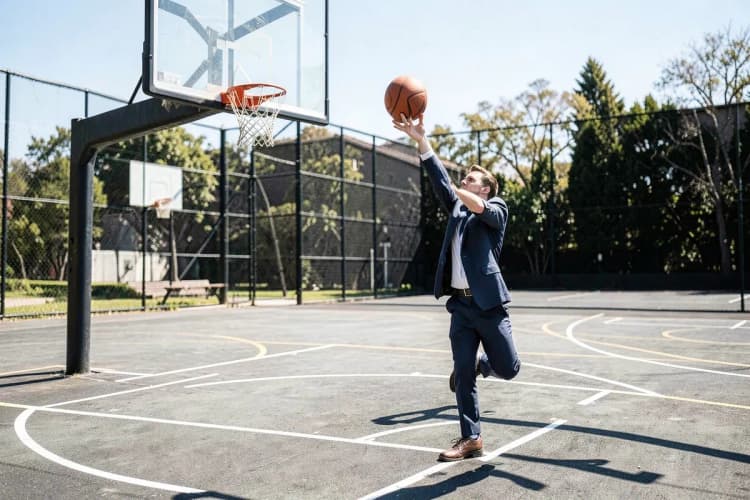 Uma pessoa jogando uma bola de basquete em uma cesta, com a bola em pleno ar.