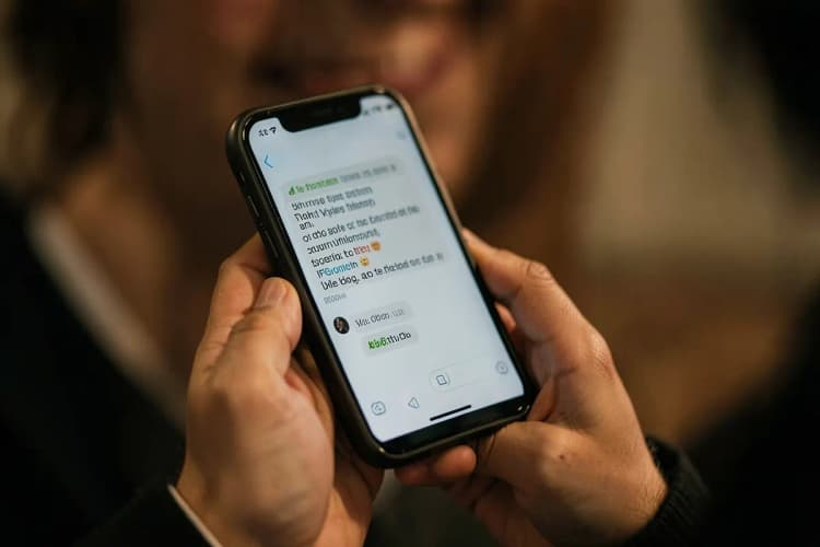 Mãos segurando um smartphone com uma mensagem de texto na tela, com um sorriso sutil ao fundo.