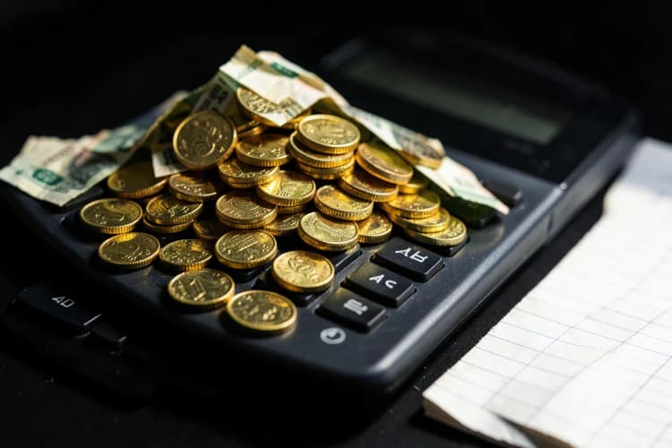 Uma pilha de moedas de ouro e notas de dinheiro em cima de uma calculadora e um pequeno bloco de notas.