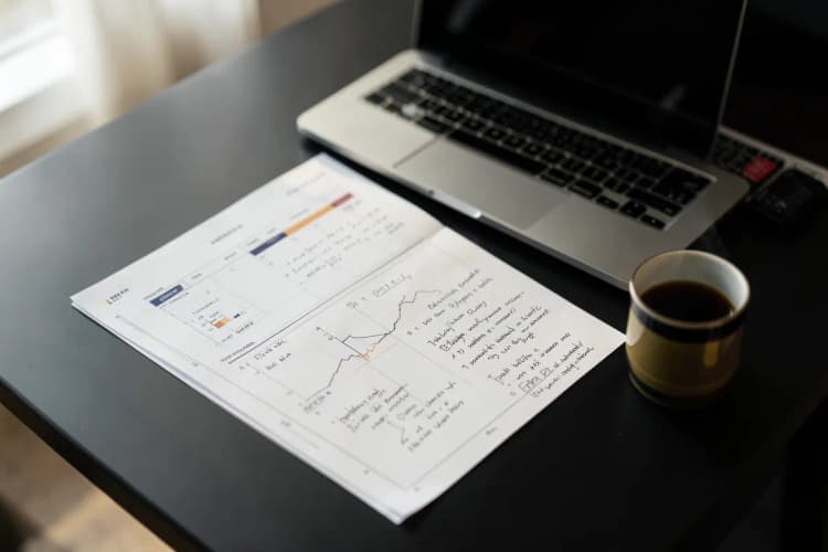 Um plano de negócios com gráficos e anotações em uma mesa com um laptop e um café.