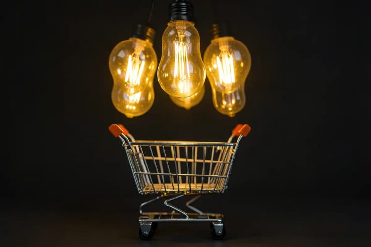 Um conjunto de lâmpadas incandescentes acesas acima de um carrinho de compras de e-commerce, representando ideias e estratégias.